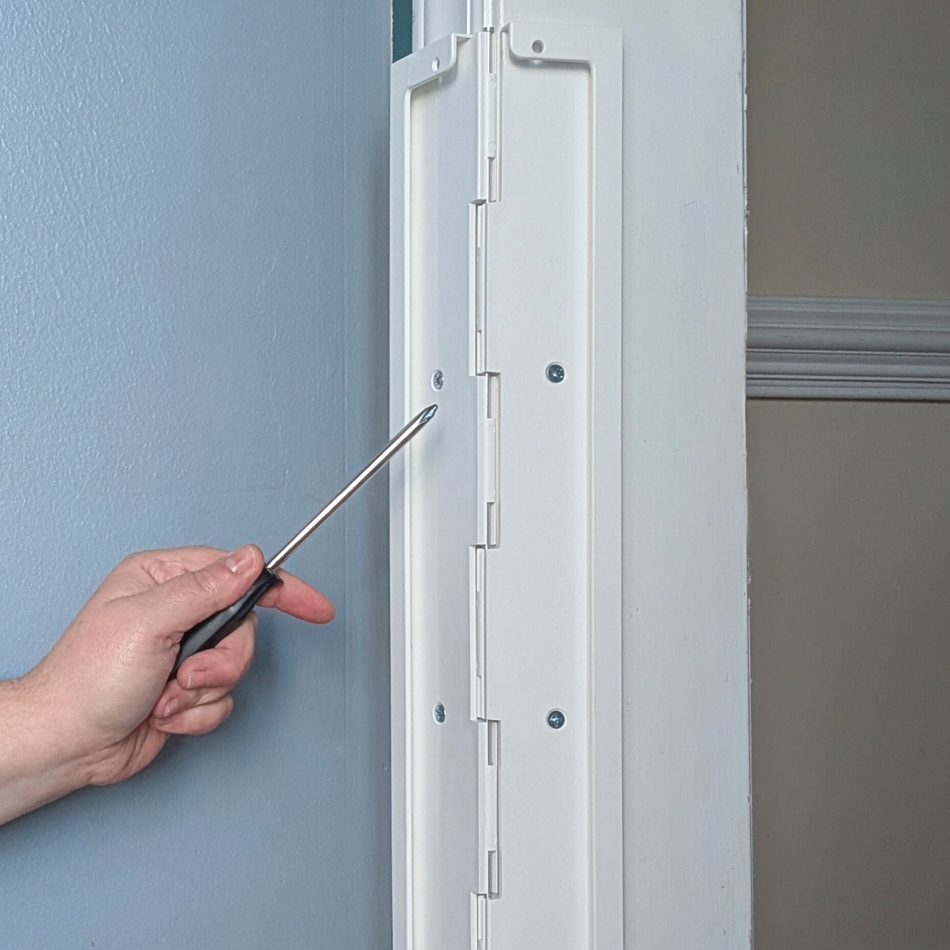 Hand holding a screwdriver in front of Jack's Scratcher attached to a door frame.