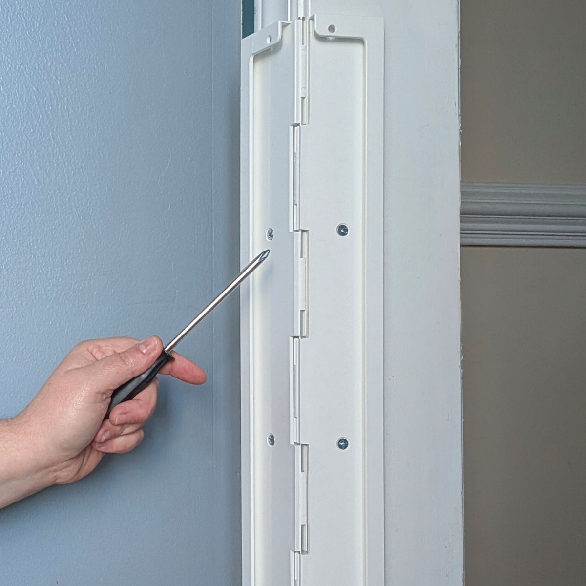 Hand holding a screwdriver in front of Jack's Scratcher attached to a door frame.