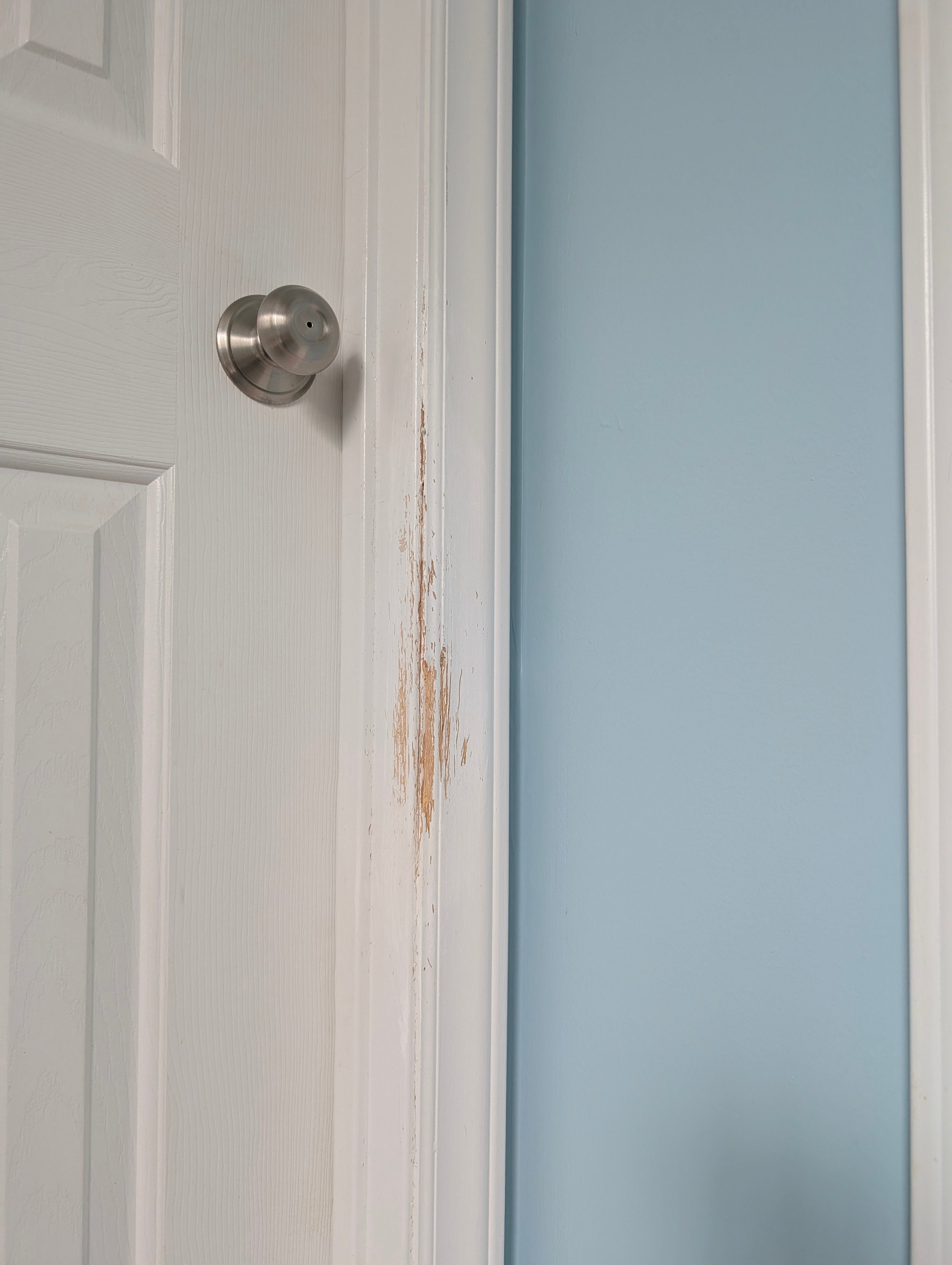 Close-up of a white door with scratched trim and a blue wall.